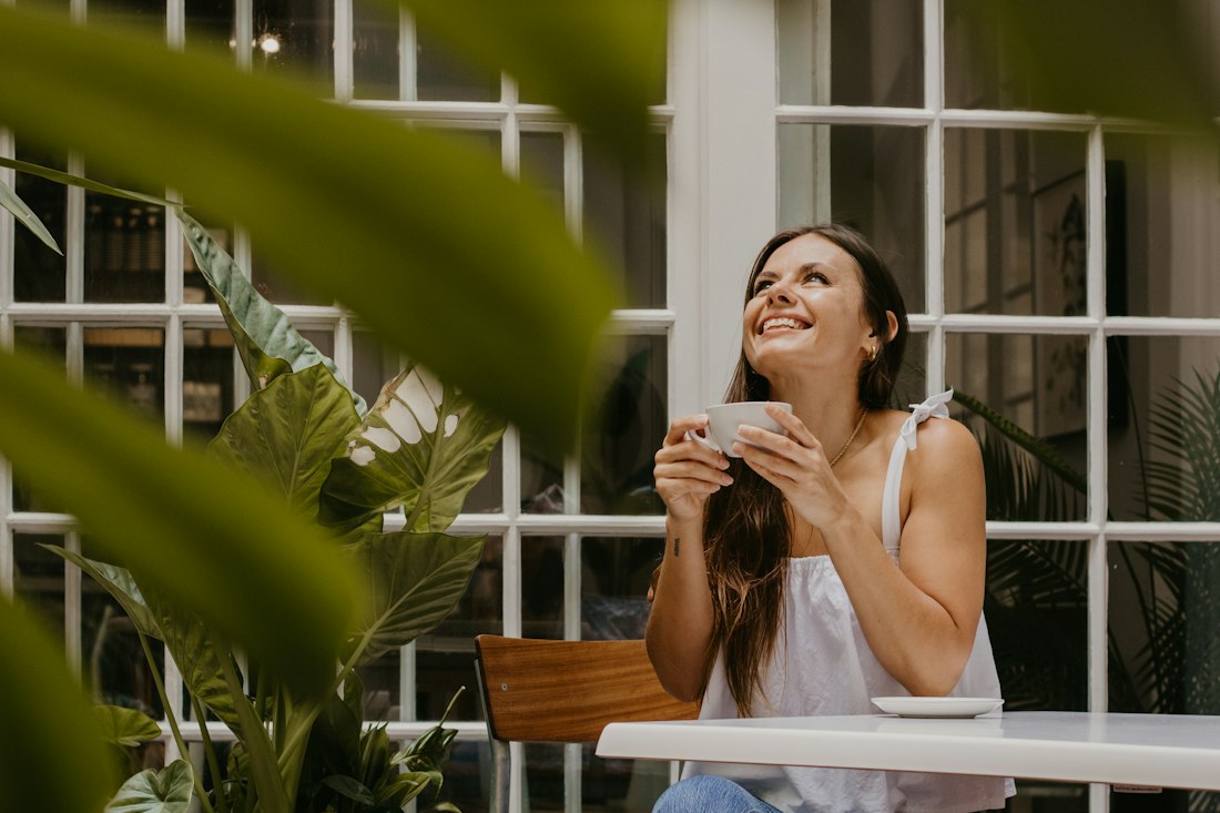 A woman smiling over a cup of coffee in a sunny café